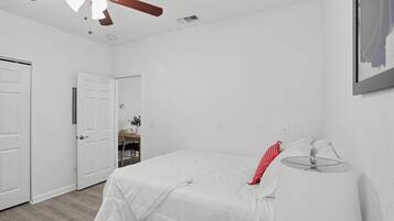 Quarto com cama, abajur, ventilador de teto e porta para outro cômodo.
