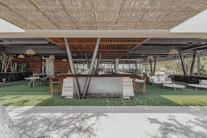 Et udendørs opholdsområde med borde og stole, en træpergola og et skilt med teksten 'FORESTA'.