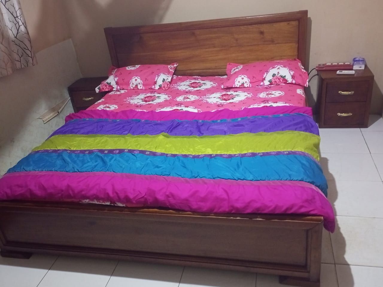 Ein Bett mit Holz Kopfteil, einer farbenfrohen Tagesdecke und einem Nachttisch mit Schubladen.