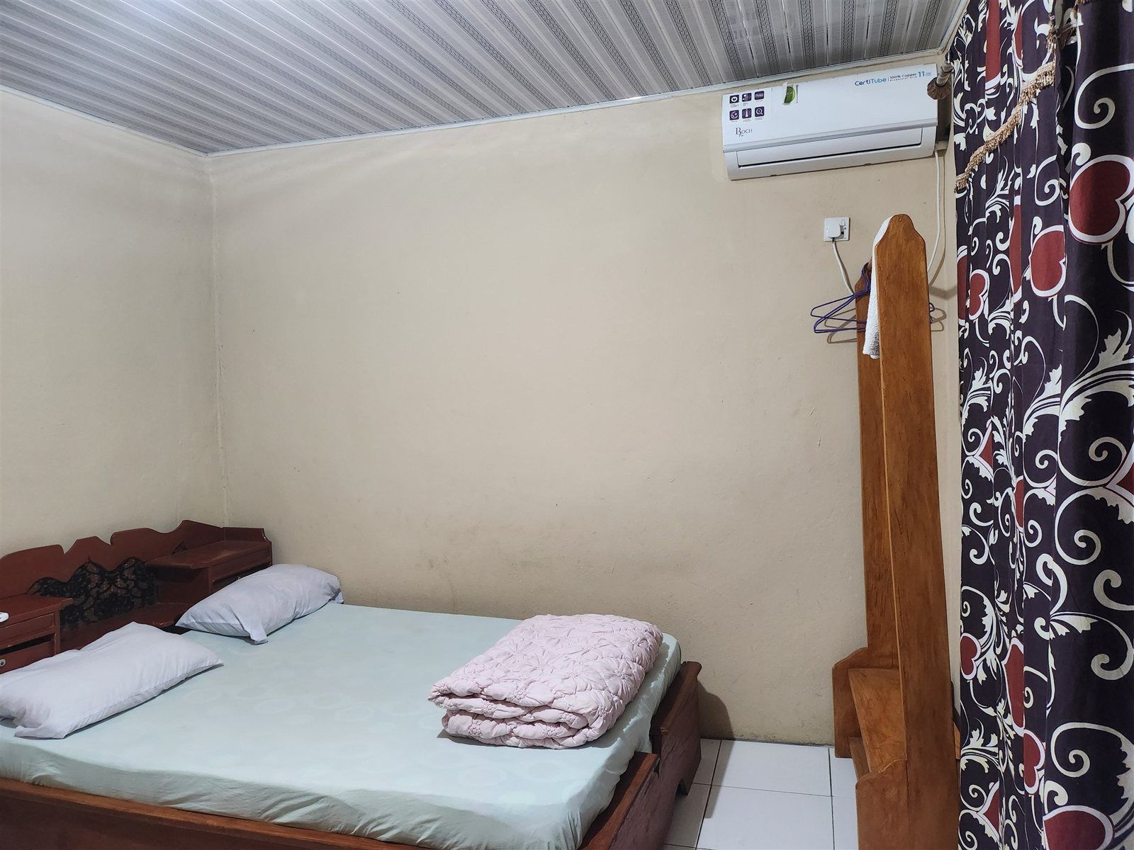 A single bed with a wooden headboard, a bedside table, and a wall-mounted air conditioner.