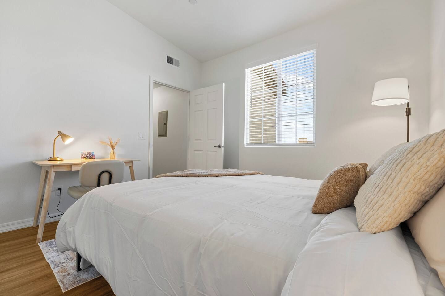 Une chambre à coucher comprenant un lit, un bureau, une chaise, une lampe et une fenêtre avec des stores.