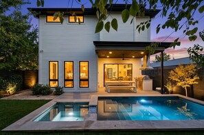 A modern two-story house with a pool, a patio, and a well-lit interior. - East Austin Skyline & Pool House ~Backyard BBQ~ (Austin)