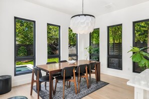 A dining area with a wooden table, black chairs, and a white pendant light. - East Austin Skyline & Pool House ~Backyard BBQ~ (Austin)