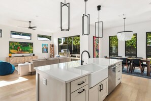 A modern kitchen with a central island, pendant lights, and artwork on the walls. - East Austin Skyline & Pool House ~Backyard BBQ~ (Austin)