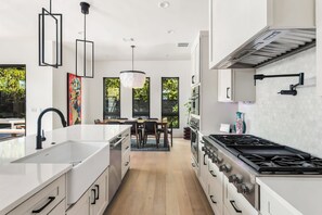 A modern kitchen with a central island, white cabinetry, and a gas stove. - East Austin Skyline & Pool House ~Backyard BBQ~ (Austin)