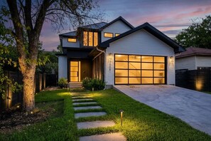 A modern two-story house with a garage, a well-maintained lawn, and a tree in the foreground. - East Austin Skyline & Pool House ~Backyard BBQ~ (Austin)