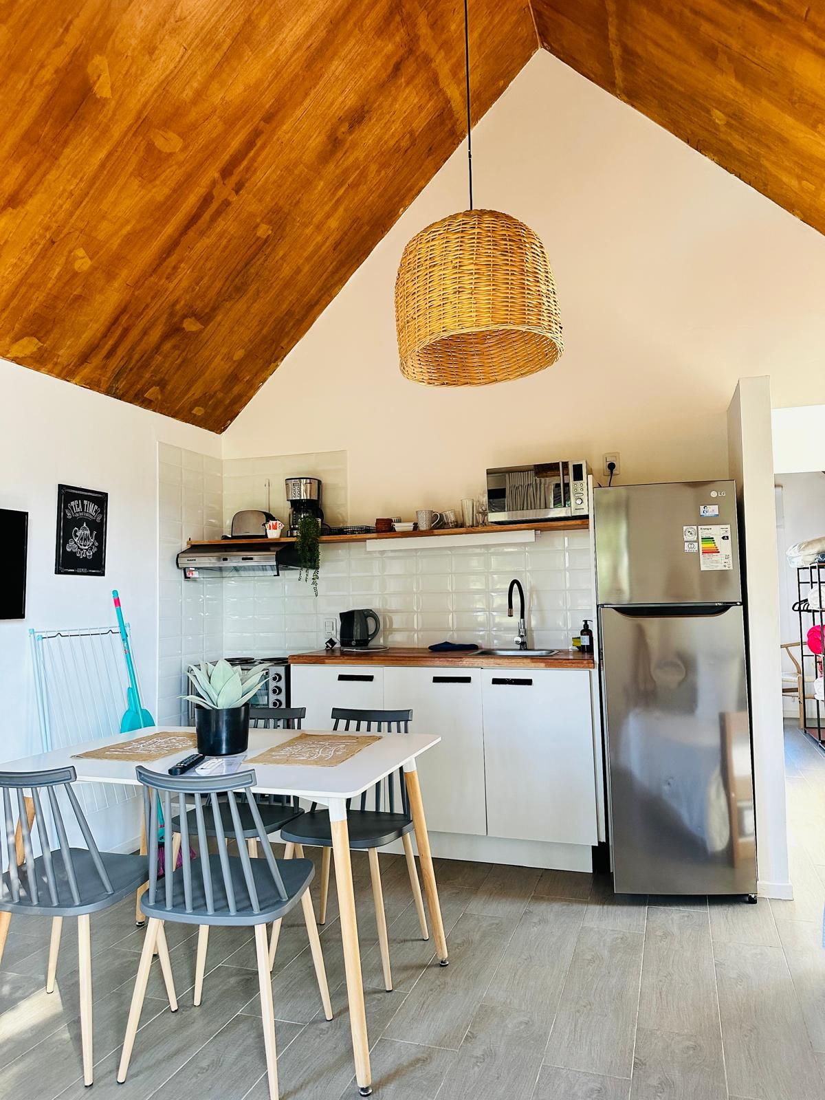 Una cocina moderna con armarios blancos, un refrigerador de acero inoxidable y una lámpara colgante de mimbre.