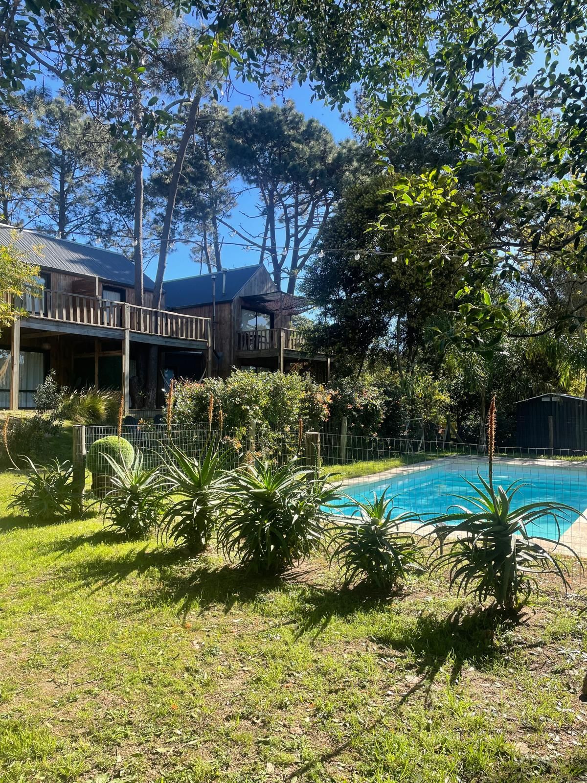 Una casa de madera con terraza y piscina, rodeada de follaje.