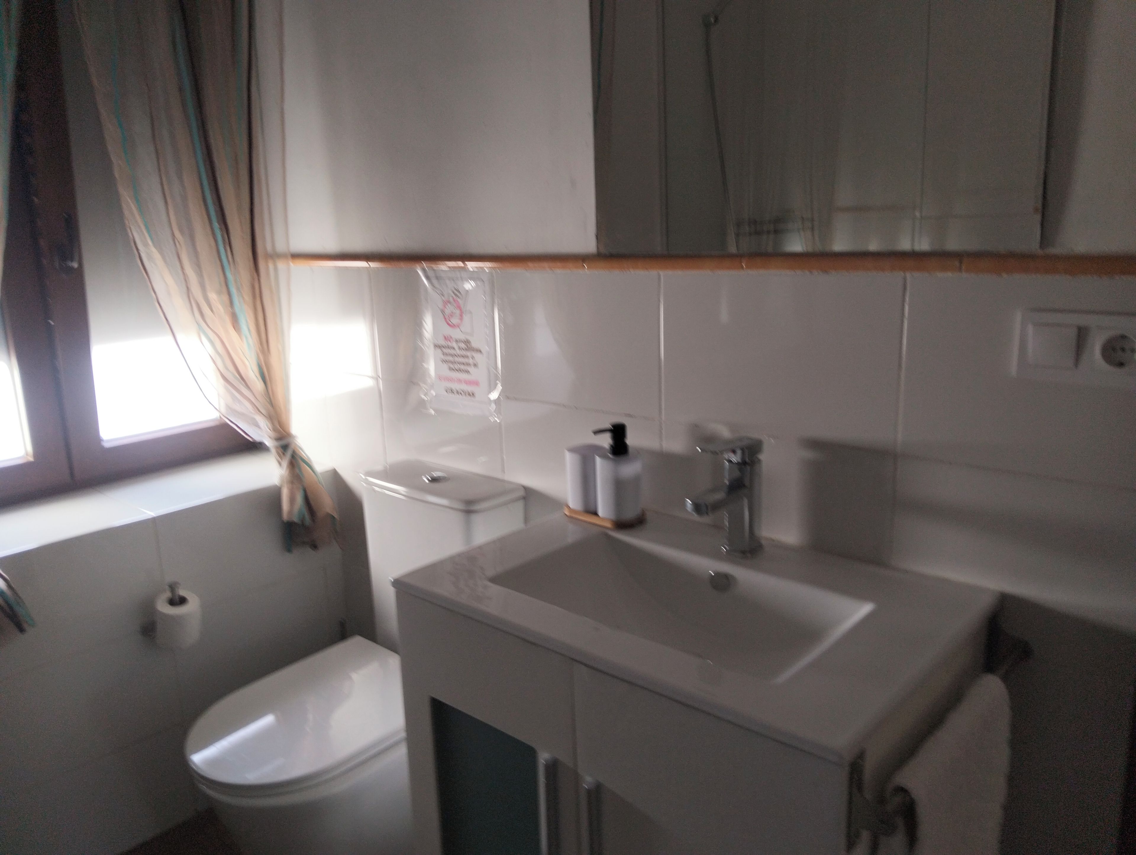 Un baño con inodoro, lavamanos y ventana con cortinas.