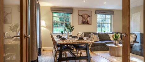 A dining area with a wooden table, chairs, and a view of the outdoors through large windows.
