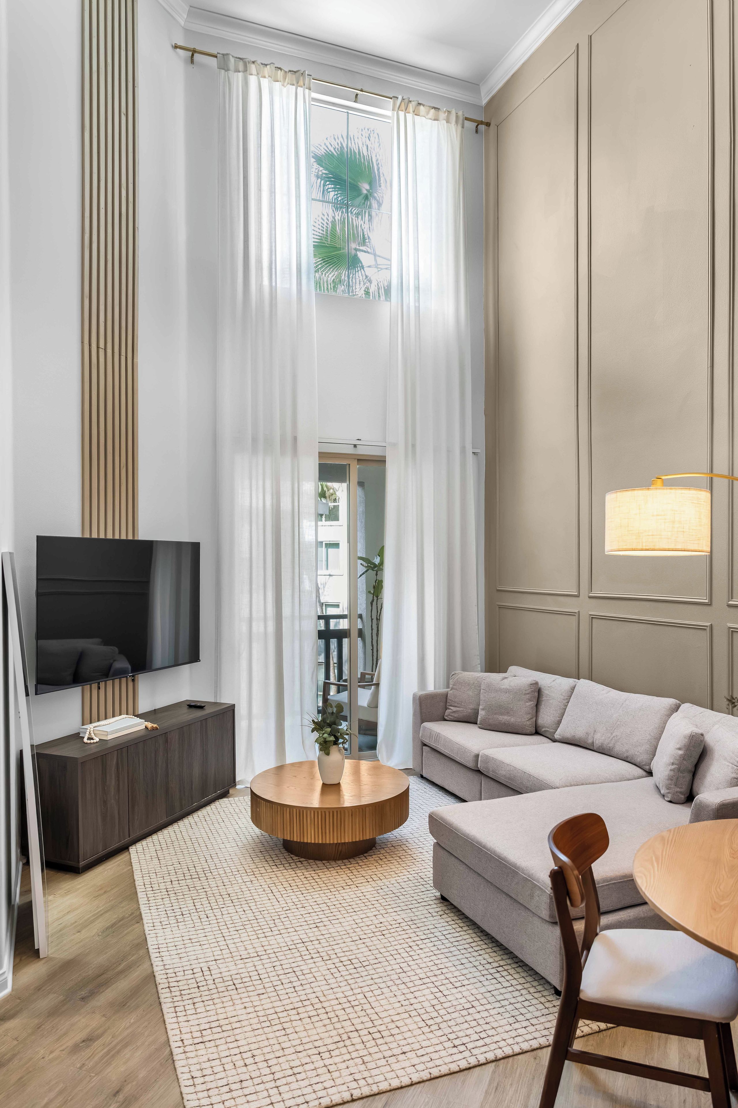 A modern living room with a sofa, a round coffee table, a TV, and a large window with curtains.