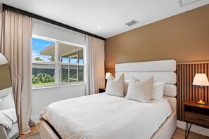 A hotel room with a large bed, a window with curtains, a bedside table with a lamp, and a wall with vertical stripes. - Experience the best of Wilton Manors (Wilton Manors)