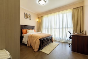 Et hotelværelse med seng, skrivebord, stol, lampe og et vindue med gardiner.