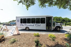 En vit buss med texten ”The Currituck Club” på sidan stod parkerad på en gata.