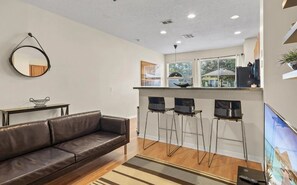 Ein modernes Wohnzimmer mit einer Ledersofa, einem kleinen Tisch und einer Küchenzeile mit Barhocker.