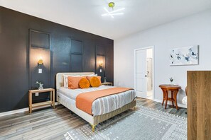 Une chambre moderne avec un lit, des tables de chevet, une commode, une porte et une petite table ronde sur laquelle est posé un vase.
