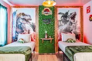 A room with two beds, dinosaur murals, a green wall with a Jurassic Park sign, and a small table with a candle. - Dino + Gamer Kids Rooms · Private Pool Resort (Clermont)