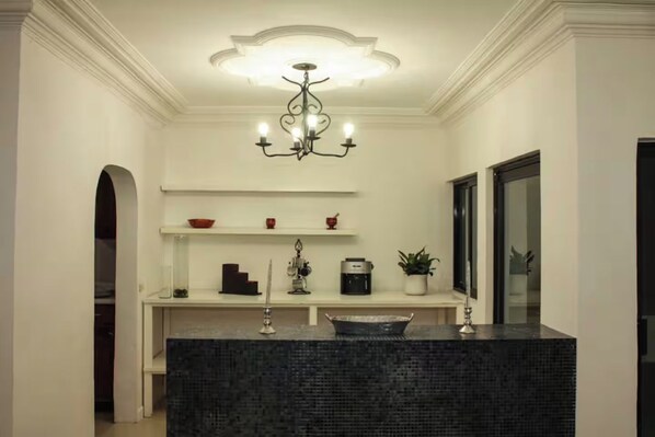 A modern bathroom with a dark marble sink, a decorative chandelier, and a mirror.
