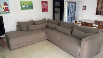 A living room with a large L-shaped sectional sofa, a flat-screen TV, and a bookshelf.