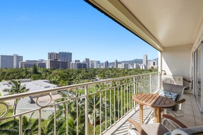 A balcony with a view of a cityscape, including high-rise buildings and palm trees. - Waikiki Oceanfront with FREE Parking & AC (Honolulu)