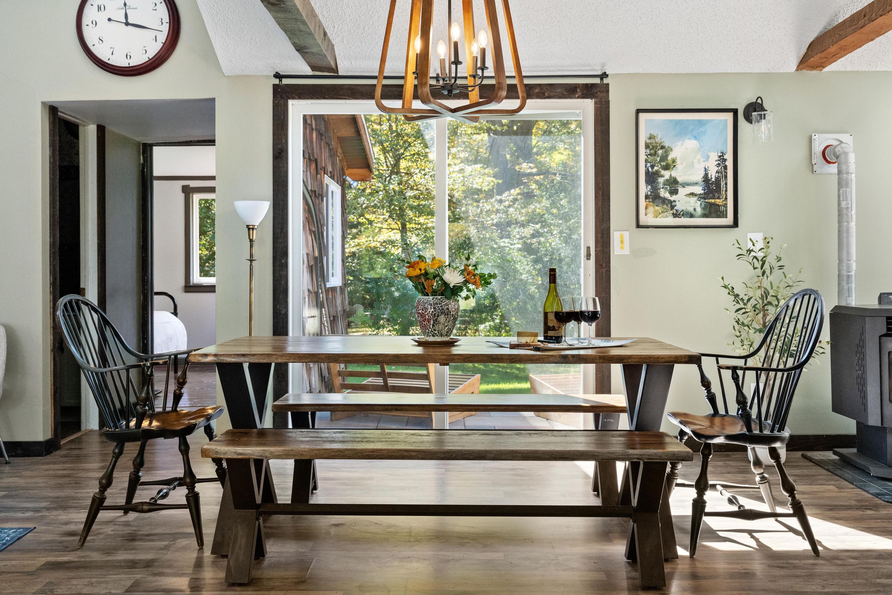 A dining area with a wooden table and benches, a vase with flowers, a wine bottle, and glasses on the table.