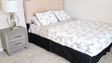 Una cama con una colcha estampada, una lámpara de noche y una mesita de noche con cajones.