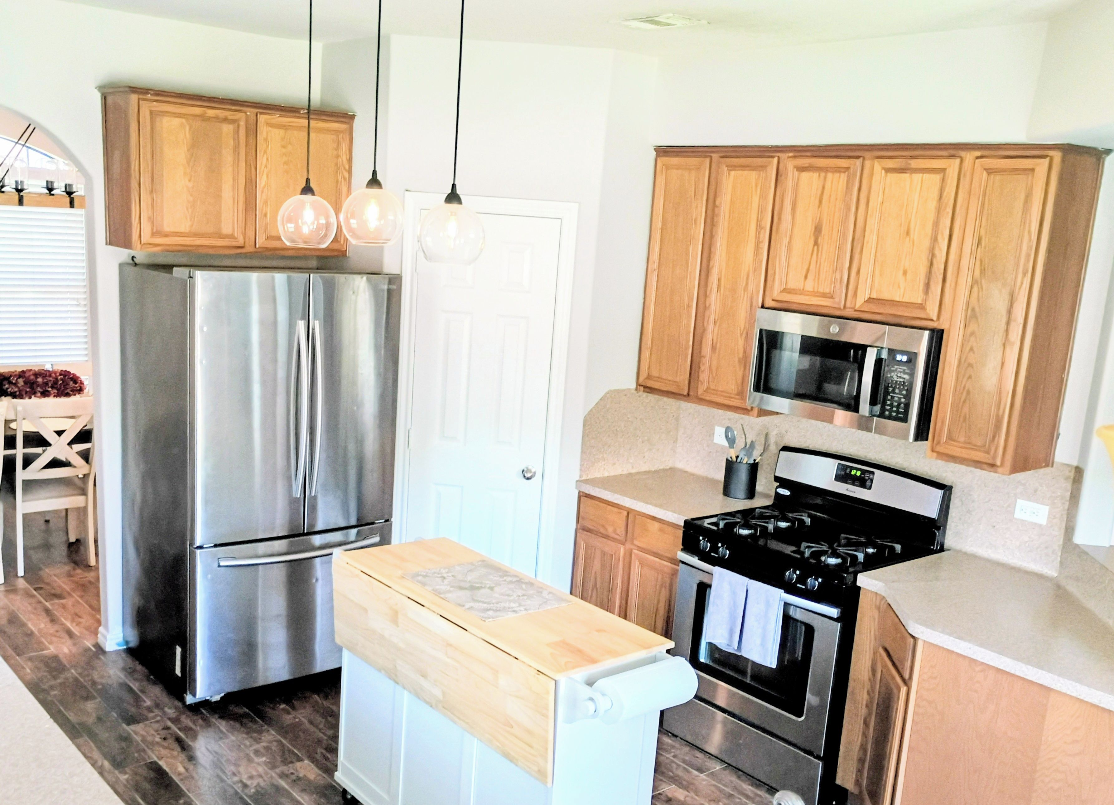 A kitchen with stainless steel appliances, wooden cabinets, and pendant lighting.