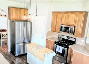 A kitchen with stainless steel appliances, wooden cabinets, and pendant lighting.