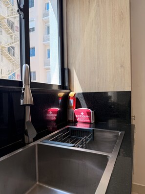 Una cocina con un lavamanos de acero inoxidable, un grifo y una ventana con vistas a un edificio.