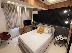 A modern hotel room with a large bed, a desk, a chair, and a small table. - Stylish 1-Bedroom Apartment in the Heart of Santo Domingo (Santo Domingo)