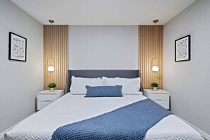 Une chambre moderne avec un grand lit, deux tables de chevet et des lampes fixées au mur.