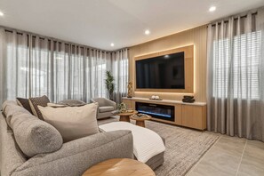 A modern living room with a flat-screen TV, a fireplace, and a comfortable seating area. - Solara 7BR | Pool, Cinema & Themed Rooms (Kissimmee)