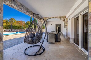 Ein überdachter Außenbereich mit einer Hängematte, einem Pool und einem Essbereich mit Korbmöbeln.