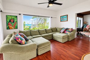 Una sala de estar con un sofá modular, un ventilador de techo y vista a la playa.