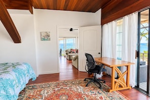 Une chambre à coucher comprenant un lit, un bureau, une chaise, un tapis à motifs et une vue sur l’extérieur, accessible par une porte coulissante.