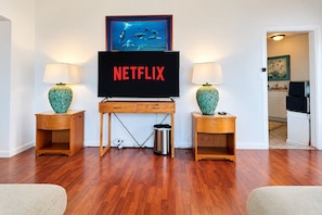 Un salon avec un bureau en bois, deux lampes, un téléviseur et un tableau encadré au mur.