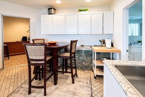 A kitchen with white cabinets, a dining table with chairs, a countertop, and a sink. - Kaneohe Bay 2BR - Oceanfront Pier & Kayaks - Wi-Fi (Kaneohe)