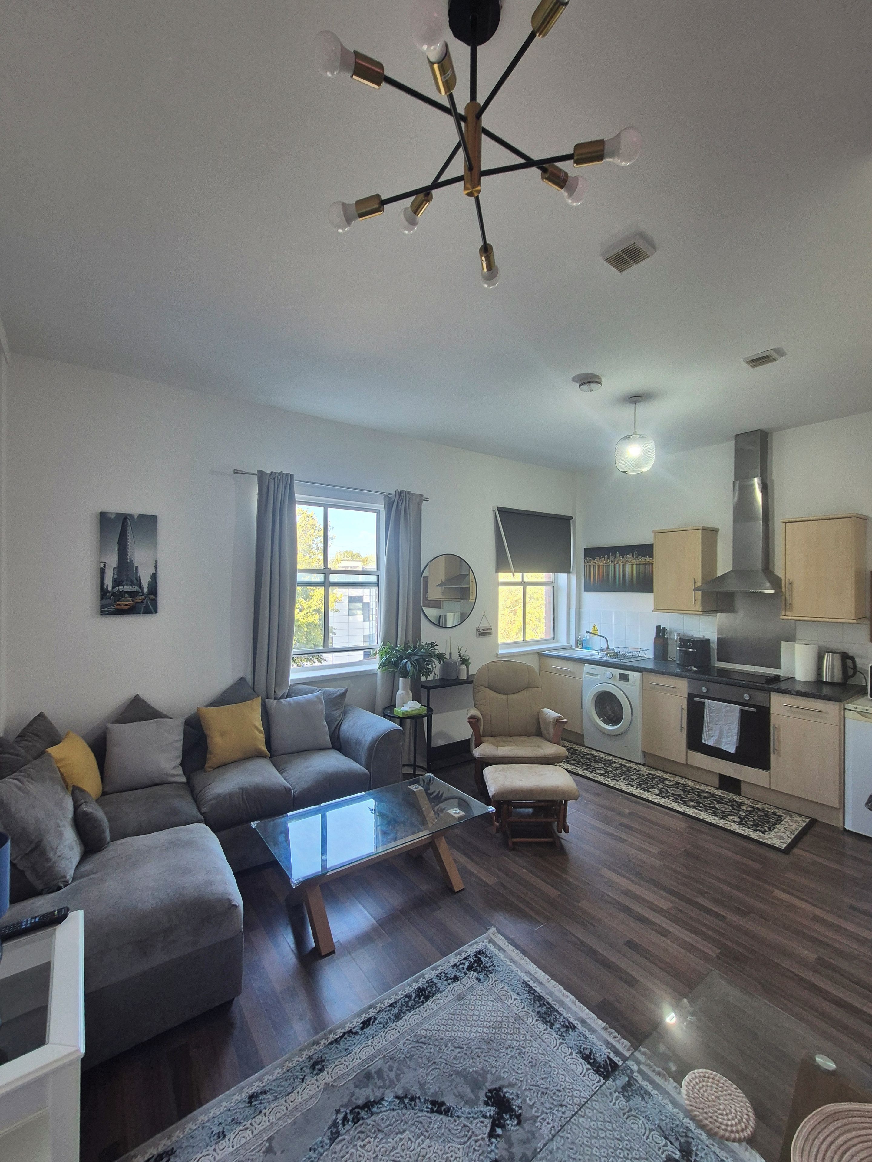 A modern living room with a sofa, coffee table, and a rug. There is a kitchen area with a stove, oven, and cabinets.