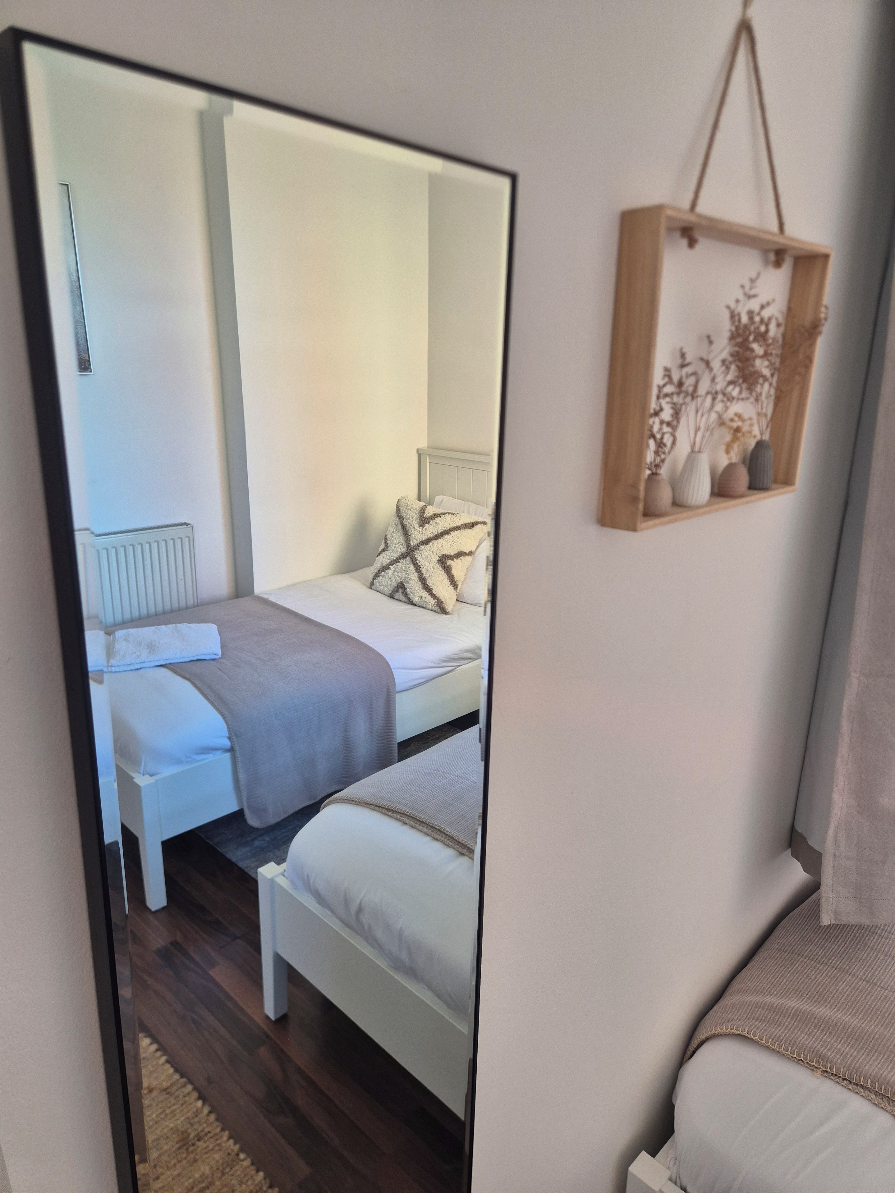 A bedroom with a bed, bedside tables, a mirror, and a wall-mounted shelf with decorative items.