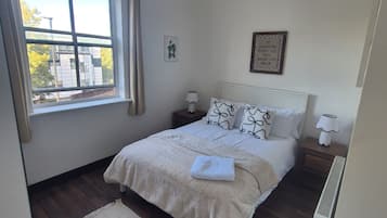 Una camera da letto con un'ampia finestra, un letto con biancheria bianca, due comodini con lampade e una citazione ispiratrice incorniciata al muro.
