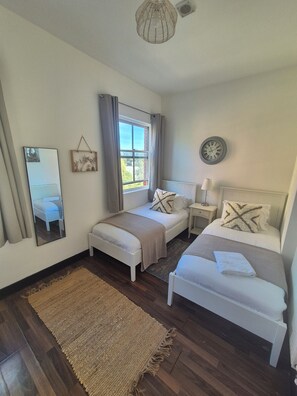Un dormitorio con dos camas, una ventana, un espejo, un reloj y una mesita de noche.