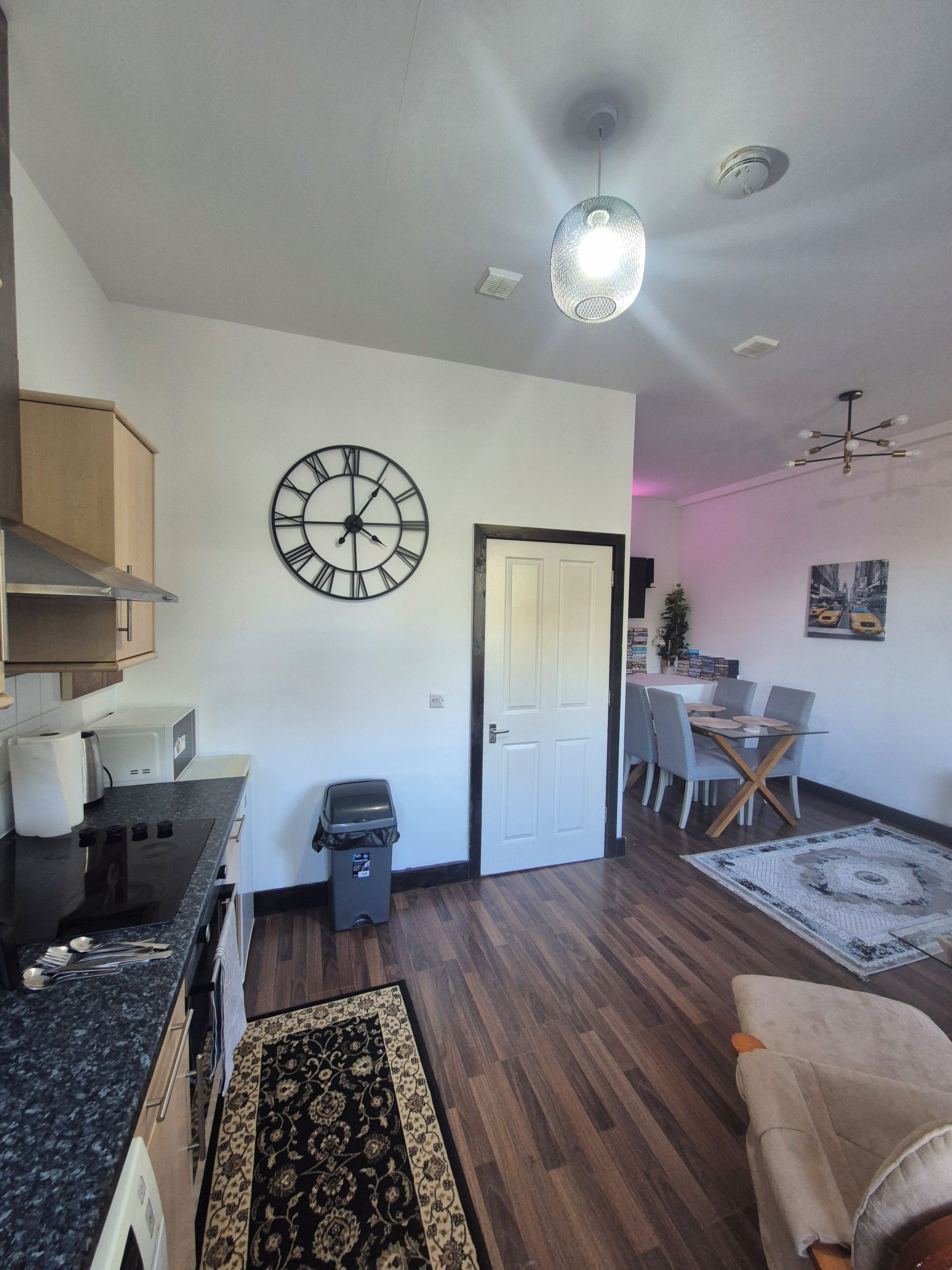 A modern living space with a kitchen, dining area, and a large wall clock.