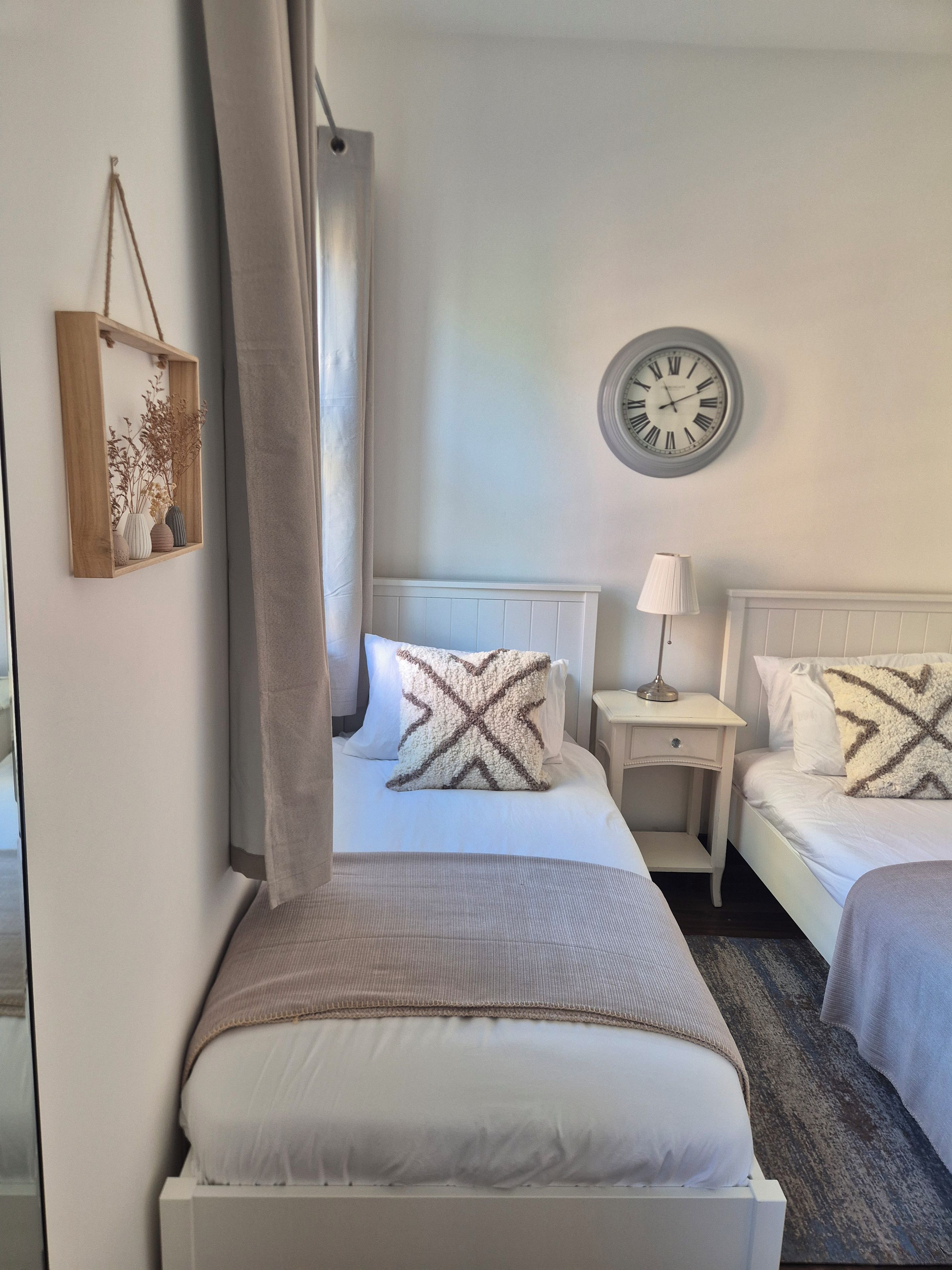 A hotel room with a bed, two bedside tables, a lamp, a clock, and a framed picture on the wall.