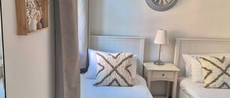 A hotel room with a bed, two bedside tables, a lamp, a clock, and a framed picture on the wall.