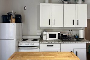 A kitchen with white cabinets, a stove, a microwave, and a sink. - Oceanfront Escape - Private Pier & Paddleboards (Kaneohe)