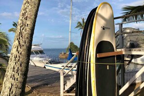 Um deck de madeira com uma prancha de surf, um barco e uma palmeira.