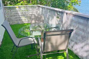 A glass-top table with metal chairs in a fenced outdoor area with grass. - Oceanfront Escape - Private Pier & Paddleboards (Kaneohe)