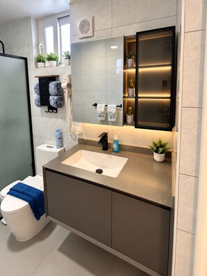 Un baño moderno con un espejo grande, un lavamanos y un inodoro.