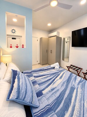 A hotel room with a bed, a ceiling fan, a flat-screen TV, a wardrobe, and a mirror. - Paradise Studio Aruba 2 (Noord)
