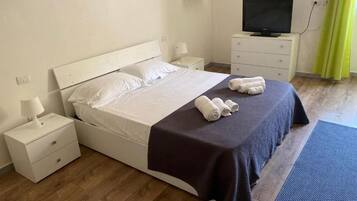 A hotel room with a bed, a TV, a bedside table, and a lamp.